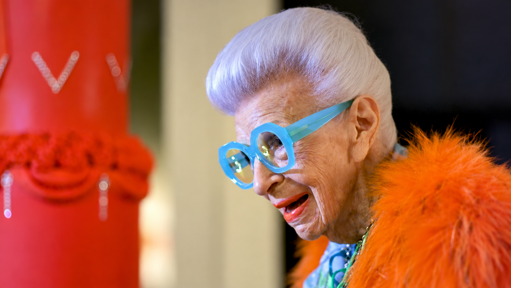 Iris Apfel wearing blue glasses and orange feathers